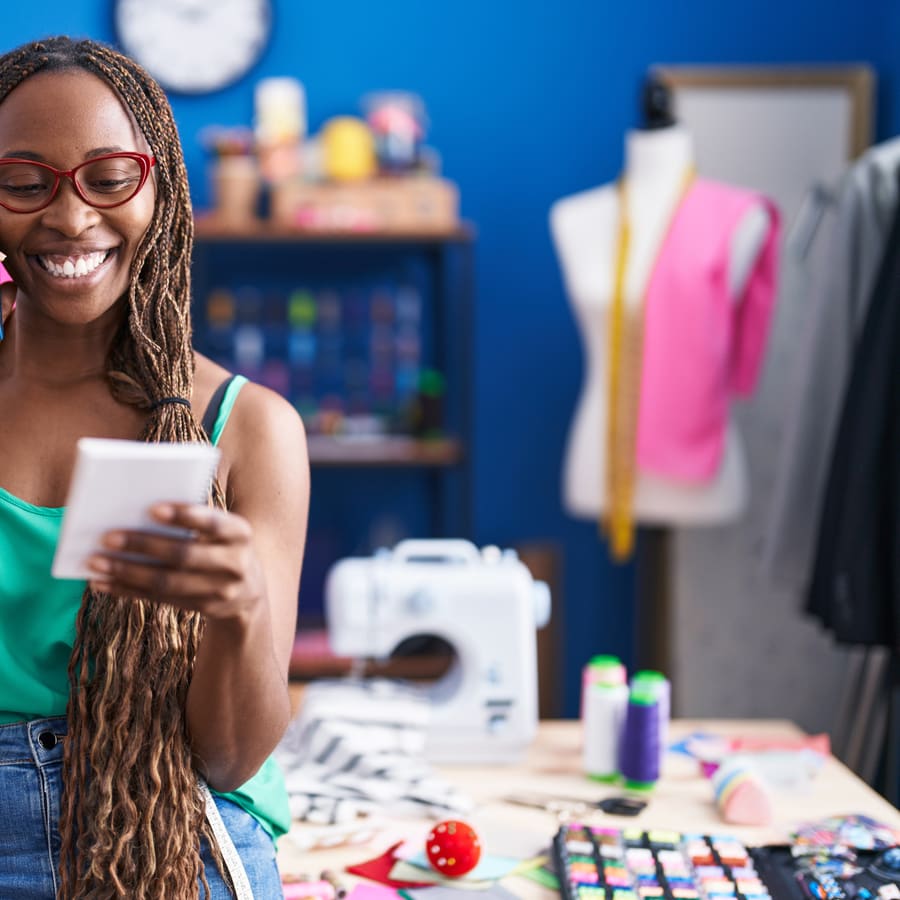 A dressmaker smiling at her phone in her workshop, with a sewing machine and a mannequin behind her